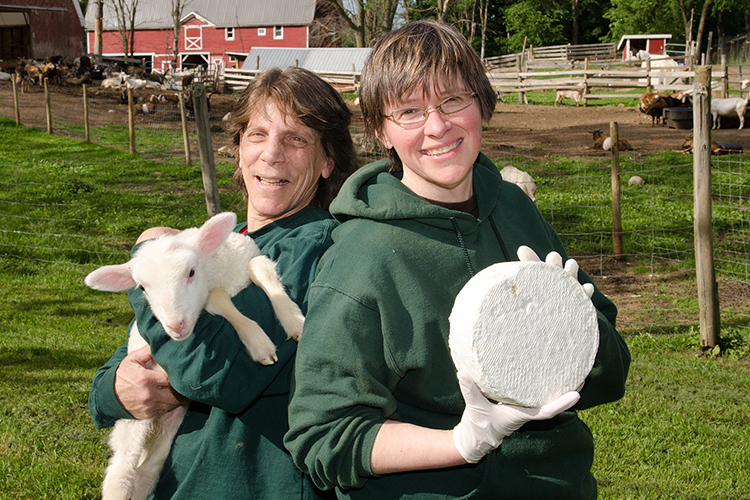 Lorraine and Sheila smiling with a goat and goat cheese