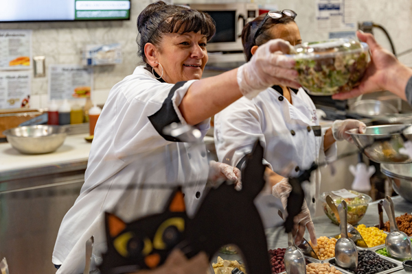 Deli counter worker handing a customer their salad